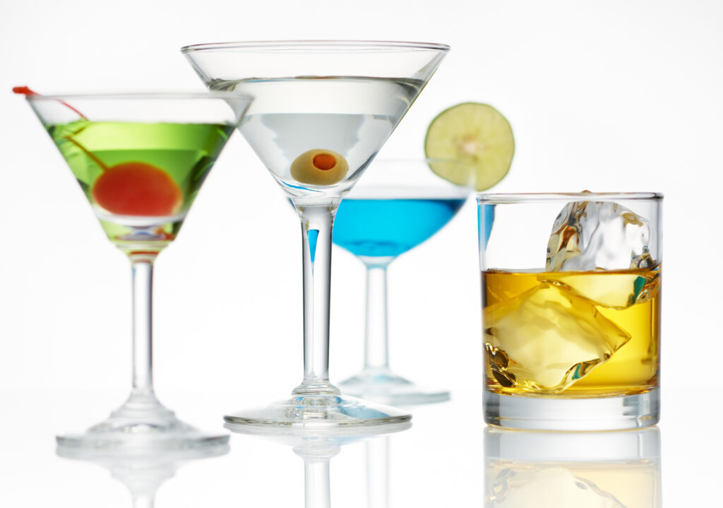 Four different alcoholic drinks—spirits and cocktails—lined up on a glass surface, illustrating the variety in alcohol, sugar, and calorie content to support mindful drinking during menopause.