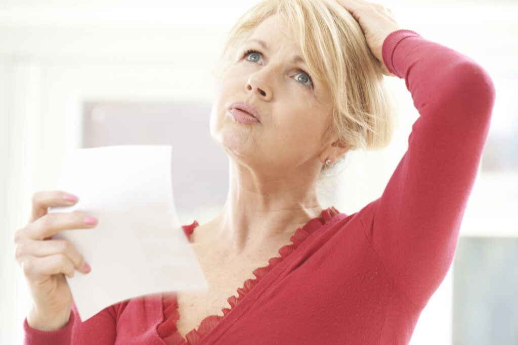 Middle-aged woman experiencing a hot flush during menopause, using a piece of paper to cool herself.