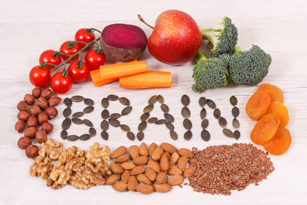 Word “brain” spelled out in pumpkin seeds, surrounded by fruits, vegetables, wholegrains, nuts, and seeds, representing nutrient-rich foods that support mood and brain health.