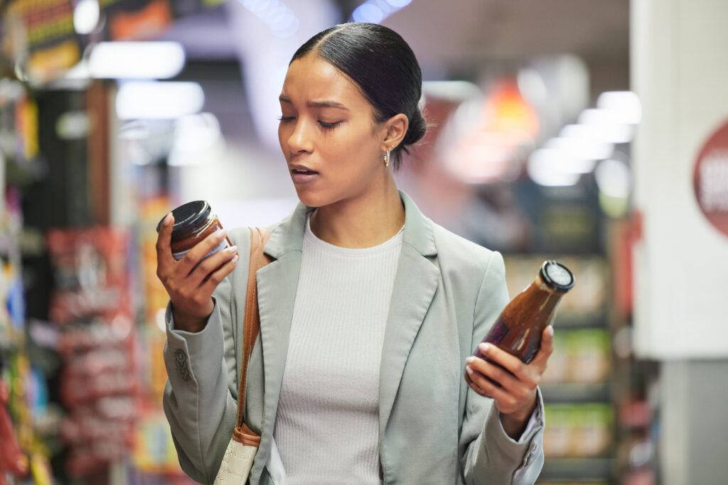 Woman comparing food labels on two jars, illustrating that the level of processing doesn’t always reflect a food’s nutritional quality.