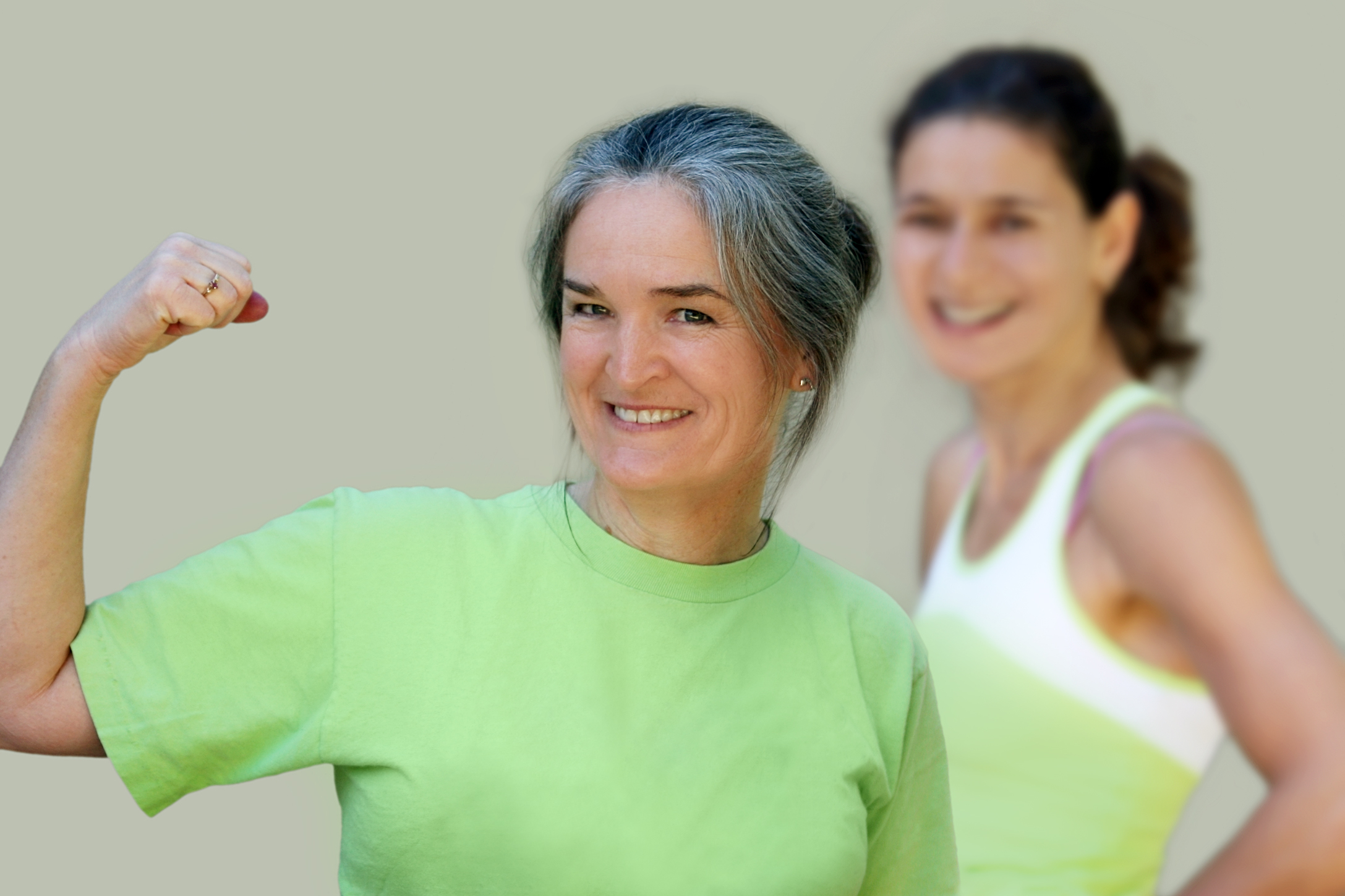 Smiling midlife woman flexing her arm muscles, illustrating the importance of maintaining strength and muscle mass during and after menopause.
